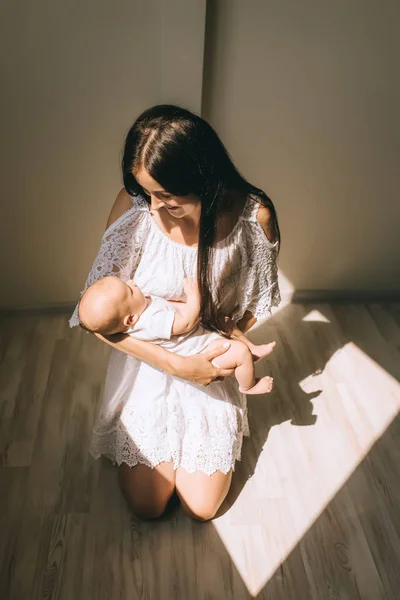 Bela mãe segurando bebê e de pé sobre joelhos de chão em casa — Fotografia de Stock