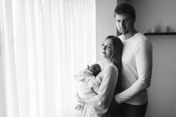 Black and white picture of family carrying little baby boy in front of curtains at home — Stock Photo
