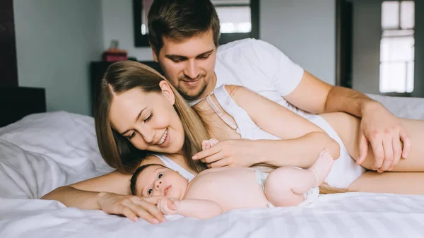 Cheerful family laying with adorable little baby son in bed at home — Stock Photo