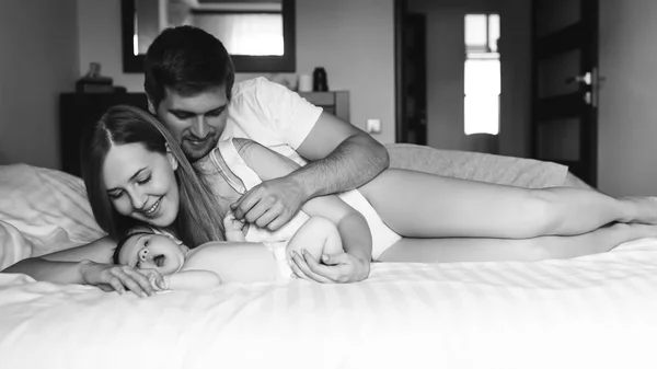 Smiling family laying with adorable little baby son in bed at home, black and white — Stock Photo