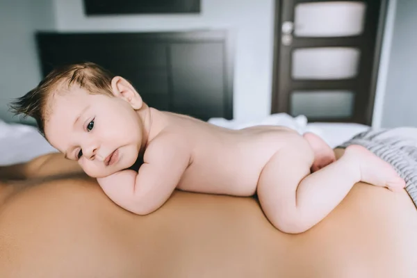 Selective focus of infant boy laying on father back in bed at home — Stock Photo