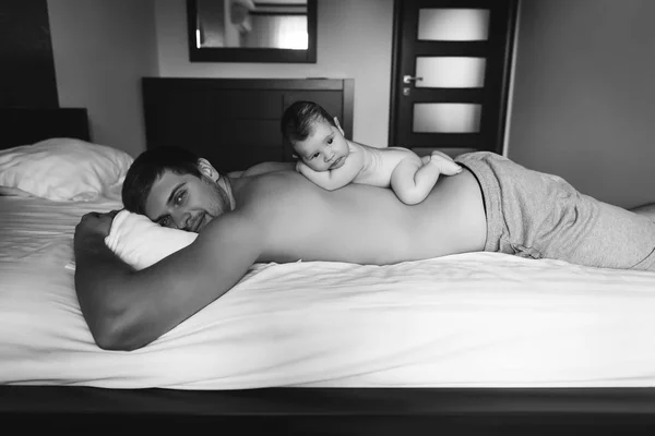 Black and white picture of infant boy laying on father back in bed at home — Stock Photo