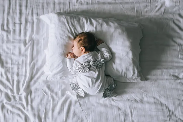 Вид сверху на маленького мальчика в костюме с крыльями, лежащими в постели дома — стоковое фото