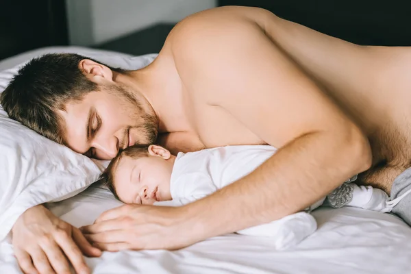 Foyer sélectif de l'homme torse nu dormant avec un enfant fils au lit à la maison — Photo de stock