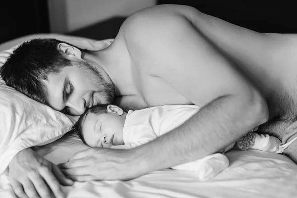 Imagen en blanco y negro del hombre sin camisa durmiendo con su hijo en la cama en casa - foto de stock
