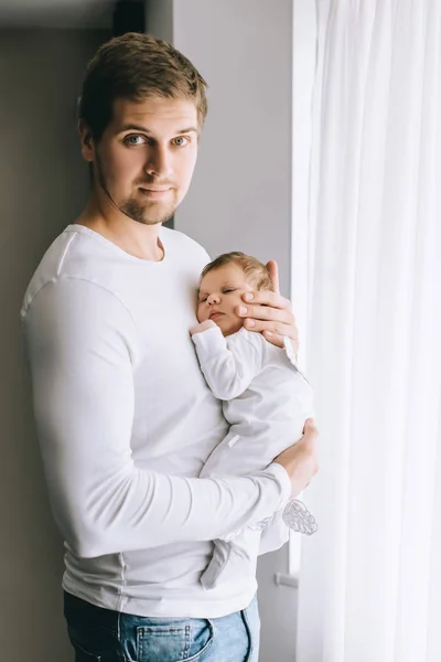 Retrato del padre llevando al niño pequeño delante de las cortinas en casa - foto de stock