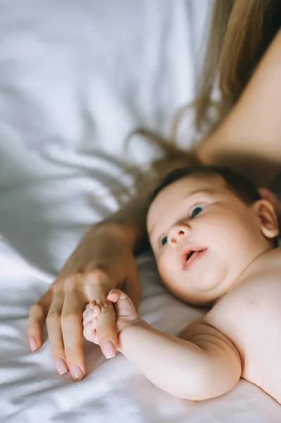 Image recadrée de la mère tenant la main du petit garçon au lit à la maison — Photo de stock