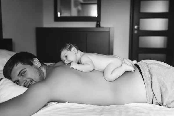 Black and white picture of adorable little baby boy laying on father back in bed at home — Stock Photo