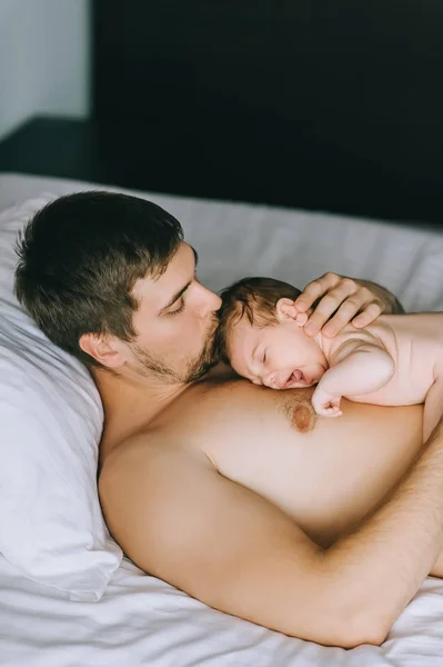 Alto ángulo vista de padre besos llorando pequeño bebé hijo en cama en casa - foto de stock