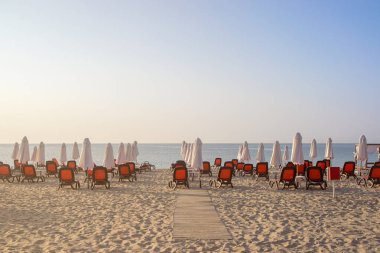 Bulgaristan'ın Karadeniz kıyısında Sunny Beach gün doğumunda güzel bir plajda sandalye ve şemsiye.