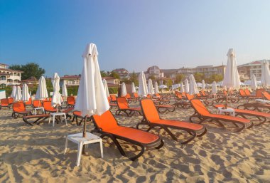 Bulgaristan'ın Karadeniz kıyısında Sunny Beach gün doğumunda güzel bir plajda kırmızı sandalye ve şemsiye.