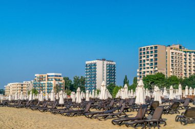 Bulgaristan'ın Karadeniz kıyısında Sunny Beach gün doğumunda güzel bir plajda sandalye ve şemsiye.