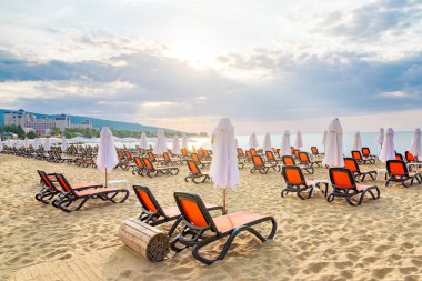 Bulgaristan'ın Karadeniz kıyısında Sunny Beach gün doğumunda güzel bir plajda sandalye ve şemsiye.