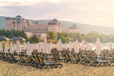 Bulgaristan'ın Karadeniz kıyısında Sunny Beach gün doğumunda güzel bir plajda sandalye ve şemsiye.