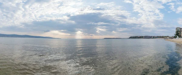 Panorama con raggi di sole o raggi di sole sbirciando tra le nuvole ad un'alba sulla bellissima spiaggia di Sunny Beach sulla costa del Mar Nero della Bulgaria — Foto Stock