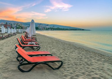 Bulgaristan'ın Karadeniz kıyısında Sunny Beach gün doğumunda güzel bir plajda sandalye ve şemsiye