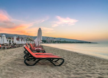 Bulgaristan'ın Karadeniz kıyısında Sunny Beach gün doğumunda güzel bir plajda sandalye ve şemsiye