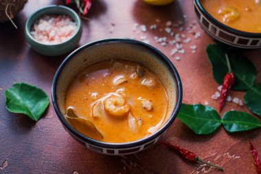 Asty Asya çorba tom yam içinde küçük kaseler, biber biber, tuz ve Hindistan cevizi ve koyu kahverengi zemin üzerine kireç