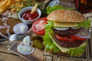 Lezzetli ev yapımı Hamburger, kızarmış patates, taze domates, marul, soğan, peynir rustik ahşap masa üzerinde. Fast food cabukşalterli, sağlıksız beslenme kavramı. Hamburger, kızarmış patates, sebze, seçici odak
