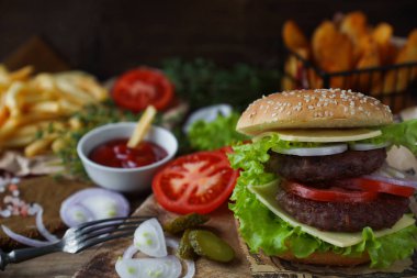 Lezzetli ev yapımı Hamburger, kızarmış patates, taze domates, marul, soğan, peynir rustik ahşap masa üzerinde. Fast food cabukşalterli, sağlıksız beslenme kavramı. Hamburger, kızarmış patates, sebze, seçici odak