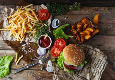 Lezzetli ev yapımı Hamburger, kızarmış patates, taze domates, marul, soğan, peynir rustik ahşap masa üzerinde. Fast food cabukşalterli, sağlıksız beslenme kavramı. Hamburger, kızarmış patates, sebze, seçici odak