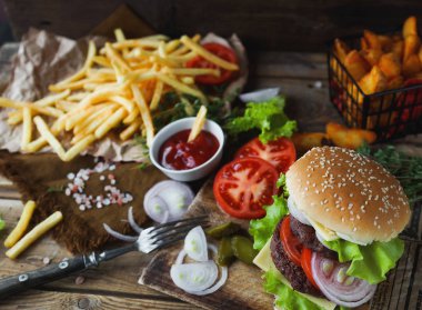 Lezzetli ev yapımı Hamburger, kızarmış patates, taze domates, marul, soğan, peynir rustik ahşap masa üzerinde. Fast food cabukşalterli, sağlıksız beslenme kavramı. Hamburger, kızarmış patates, sebze, seçici odak