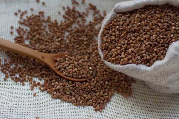 Healthy buckwheat grain in a linen bag bag and wooden spoon on light background, selective focus. Organic and nutritious meal, gluten free