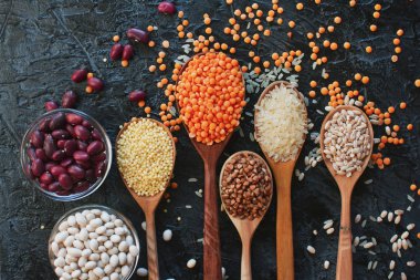 dağınık masada tahta kaşıklar ve kavanozlar içinde çeşitli tahıl üstten görünüm