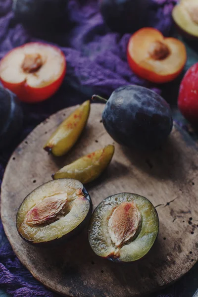 Fresh organic plums and plum slices on wooden board and rustic wooden table