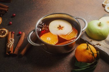 Homemade mulled wine with orange, apple and spices in aluminum casserole  clipart
