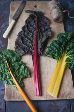 Koyu ahşap masa üzerinde taze organik gökkuşağı İsviçre pazı yaprakları, renkli sağlıklı gıda konsepti