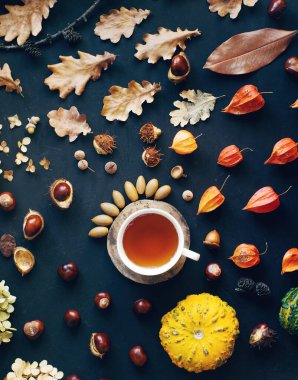 Sıcak çayla sıcak kompozisyon, kurumuş sonbahar yaprakları ve koyu taş masada fındıklar.