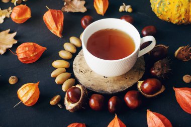 Sıcak çay, kurumuş sonbahar yaprakları ve koyu taş masada fındıklar, seçici bir odak noktası.