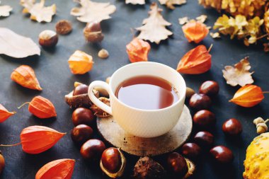 Sıcak çay, kurumuş sonbahar yaprakları ve koyu taş masada fındıklar, seçici bir odak noktası.