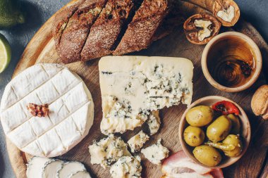 Peynir, hamon, bal, yeşil zeytin, fındık ve baharatlar sade ahşap tahtada, çeşitli mezeler koyu taş masada, üst manzara