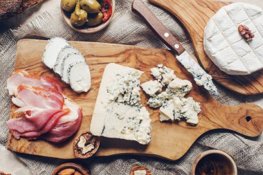 Peynir, hamon, bal, yeşil zeytin, fındık ve baharatlar sade ahşap tahtada, hafif beton masada çeşitli atıştırmalıklar, üst manzara.