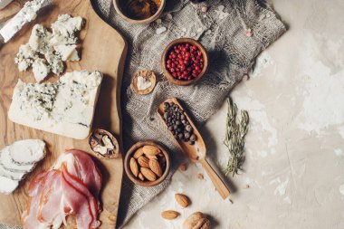 Peynir, hamon, bal, yeşil zeytin, fındık ve baharatlar sade ahşap tahtada, hafif beton masada çeşitli atıştırmalıklar, üst manzara.