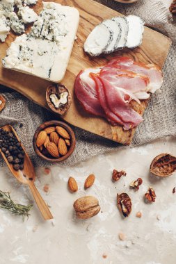 Peynir, hamon, bal, yeşil zeytin, fındık ve baharatlar sade ahşap tahtada, hafif beton masada çeşitli atıştırmalıklar, üst manzara.