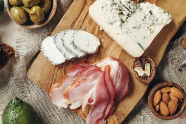Peynir, hamon, bal, yeşil zeytin, fındık ve baharatlar sade ahşap tahtada, hafif beton masada çeşitli atıştırmalıklar, üst manzara.