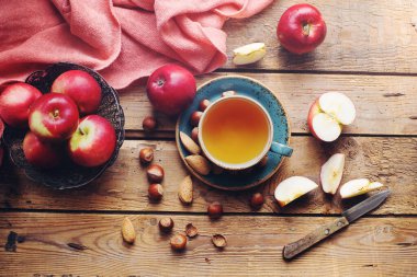 Sıcak sonbahar kompozisyonu bir fincan çay, taze elmalar ve fındıklar kırsal ahşap masa, üst manzara, seçici odak
