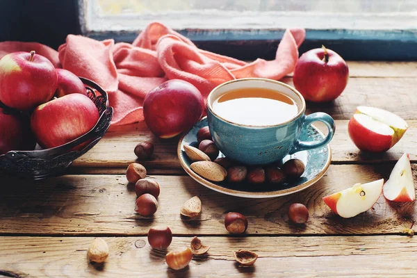Sıcak sonbahar kompozisyonu bir fincan çay, taze elma ve fındık kırsal ahşap masa üzerinde, seçici odak