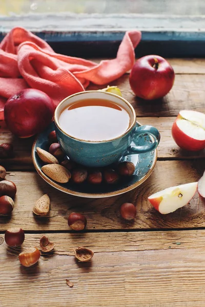 Cozy morning autumn composition with cup of tea, fresh apples and nuts on rustic wooden table, selective focus