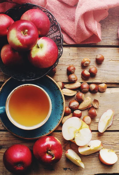 Cozy morning autumn composition with cup of tea, fresh apples and nuts on rustic wooden table, top view, selective focus