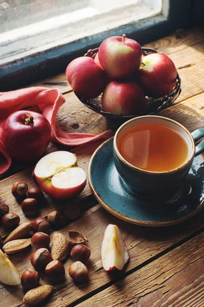 Cozy morning autumn composition with cup of tea, fresh apples and nuts on rustic wooden table, selective focus