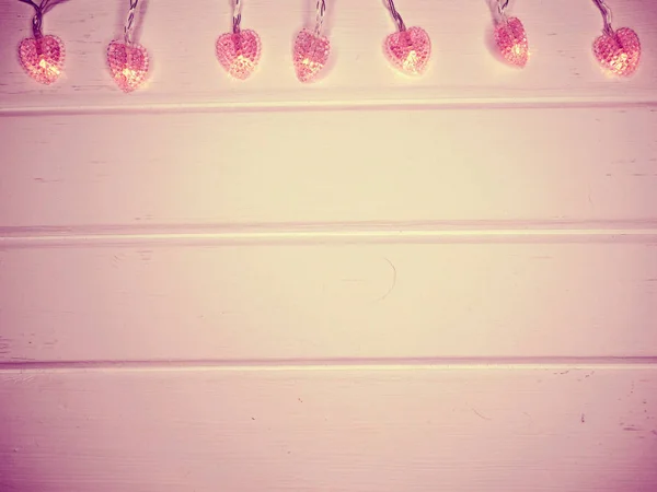 Girlanden-Herzen beleuchten Valentinstag auf weißem Holzgrund — Stockfoto