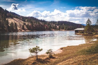 Dağlar ve ormanlarla çevrili bir gölde küçük bir kulübe.