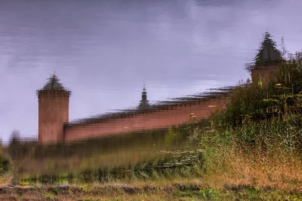 Reflection of the old fortress wall with towers, a hill and the sky in the water
