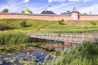 Rivulet, ahşap köprü ve tuğla manastır duvarı ile yaz kırsal peyzaj. Ortaçağ Rusya.