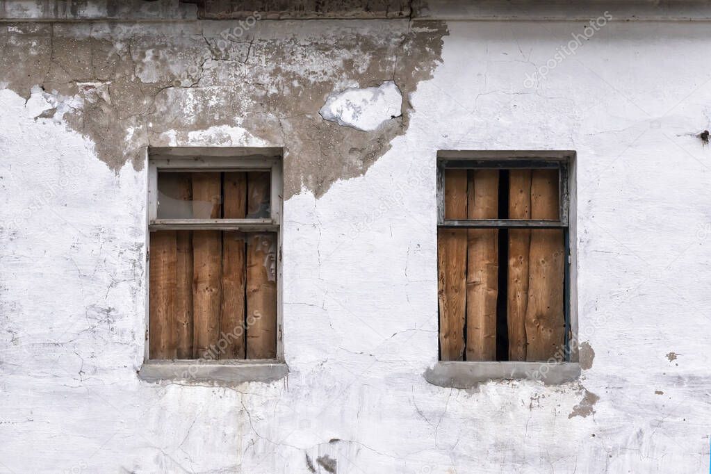 Two windows boarded up by wooden planks in a brick wall of an old building close up