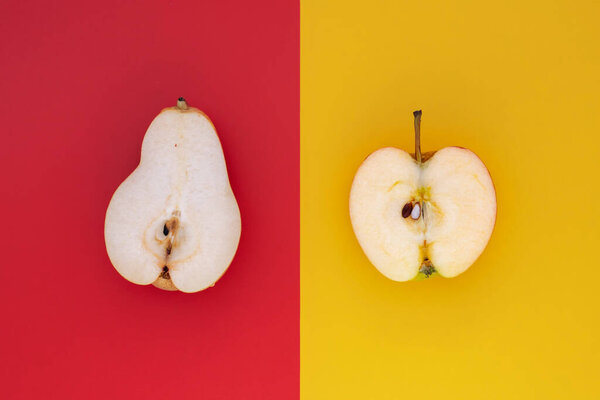 Pear vs Apple. Half a pear on red background versus half an apple on yellow background. Top view.